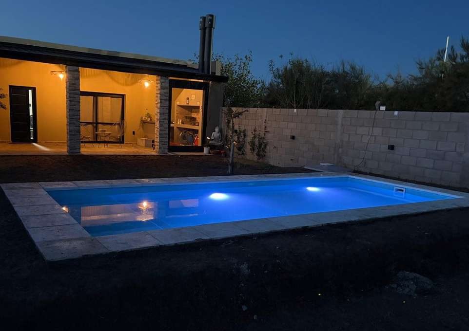Piscina iluminada con LED de noche junto a una casa moderna